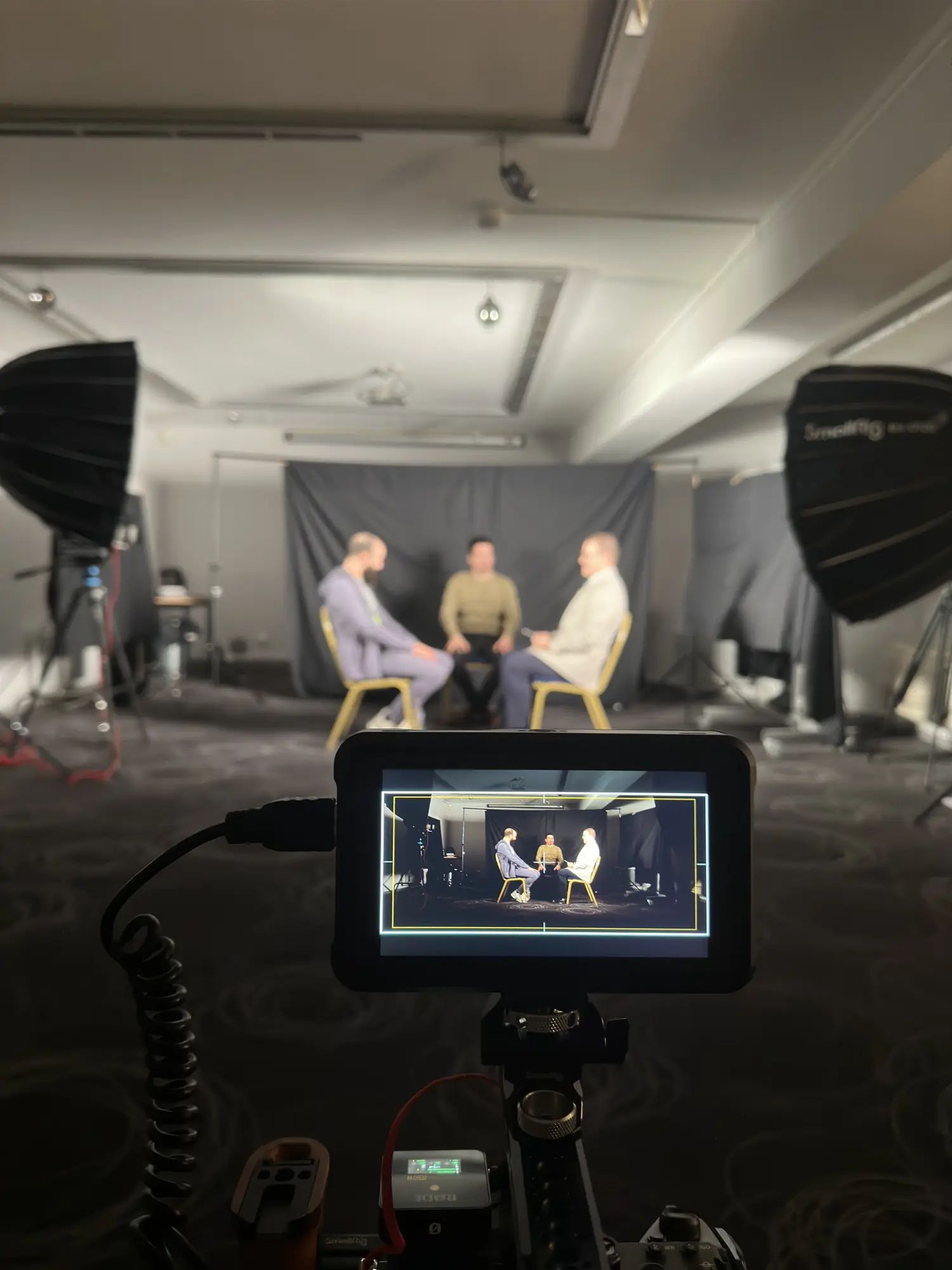 Plateau d'interview sur fond gris, trois intervenants